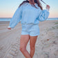 Woman in a blue checkered outfit standing on a sandy beach.