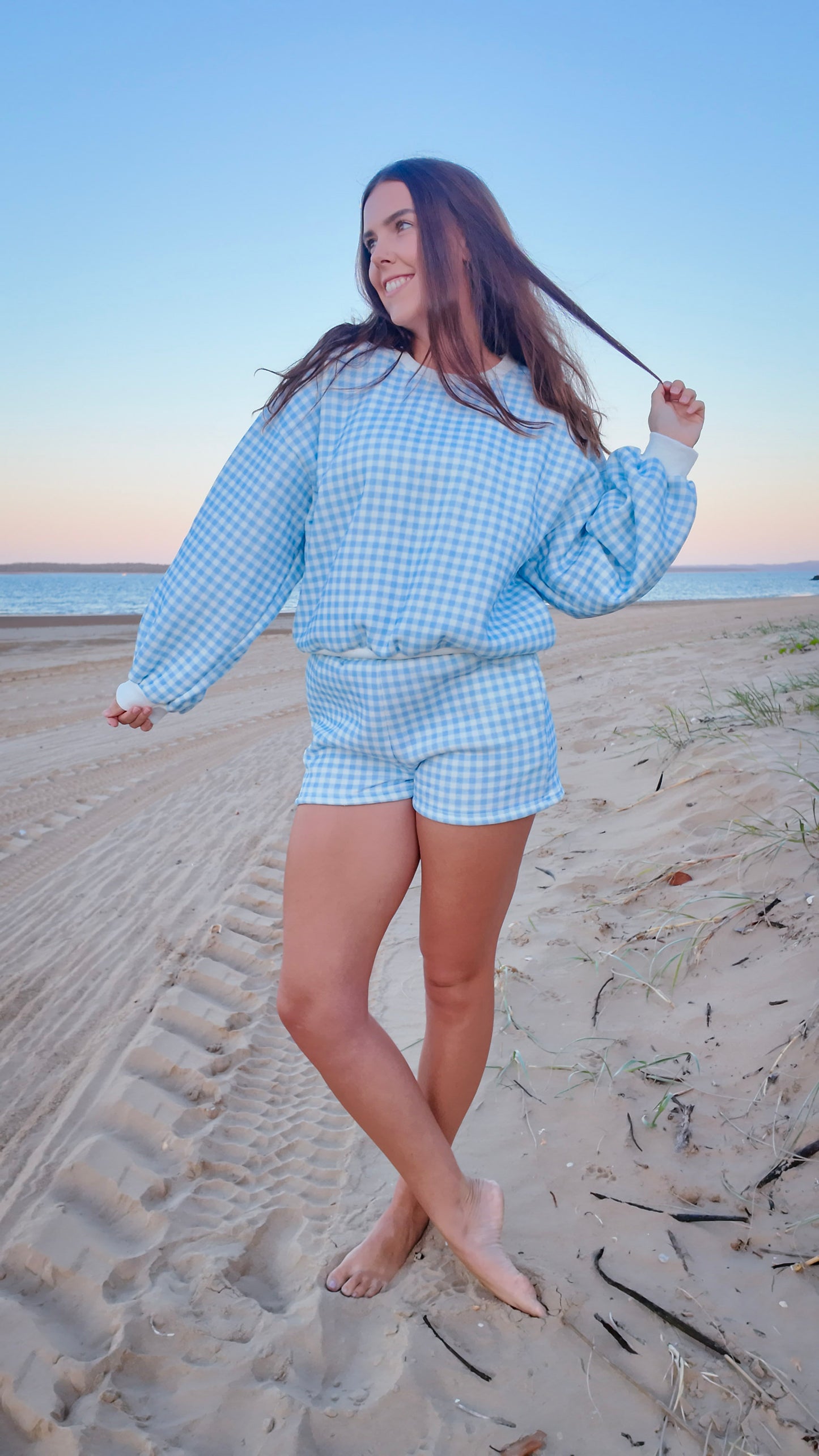 Woman in a blue checkered outfit standing on a sandy beach.