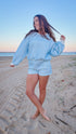Woman in a blue checkered outfit standing on a sandy beach.