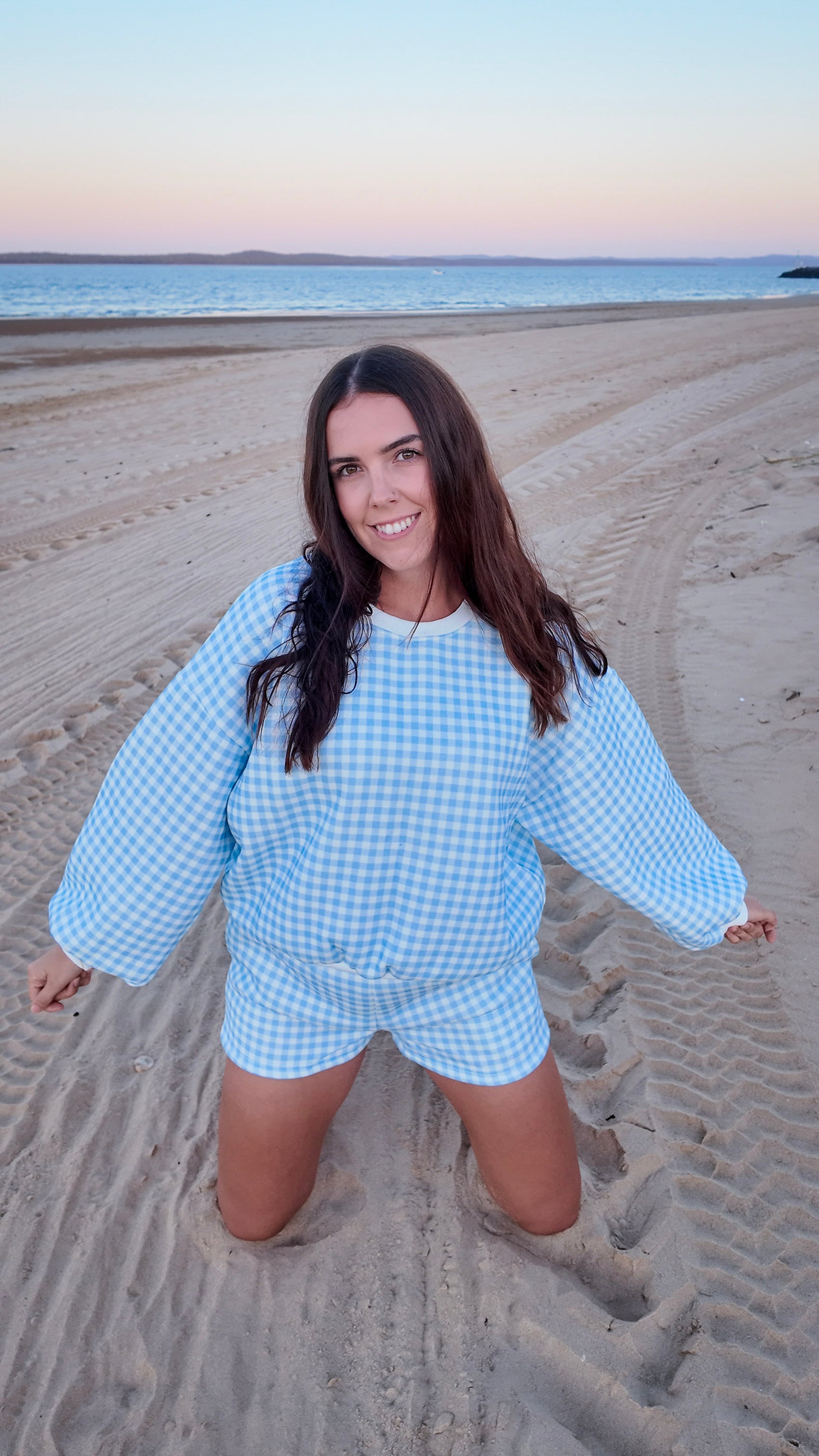 Woman in a blue checkered outfit on a sandy beach at sunset
