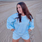 Woman in a blue checkered outfit standing on a sandy beach with ocean in the background