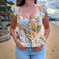 Woman wearing a colorful patterned top and denim shorts on a beach.