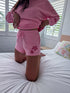 Person wearing a pink outfit with floral designs on a bed.