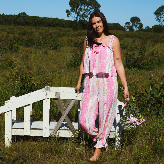 Model wearing a floral two-piece cotton pyjama set featuring a singlet top with a pink bow detail and relaxed-fit pants cuffed at the ankle, combining comfort with a feminine touch.
