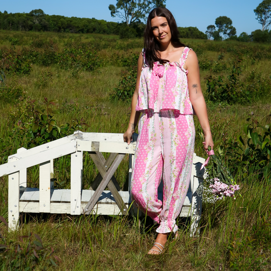 Woman in a pink floral pyjama set standing in a field with a white bench and flowers.