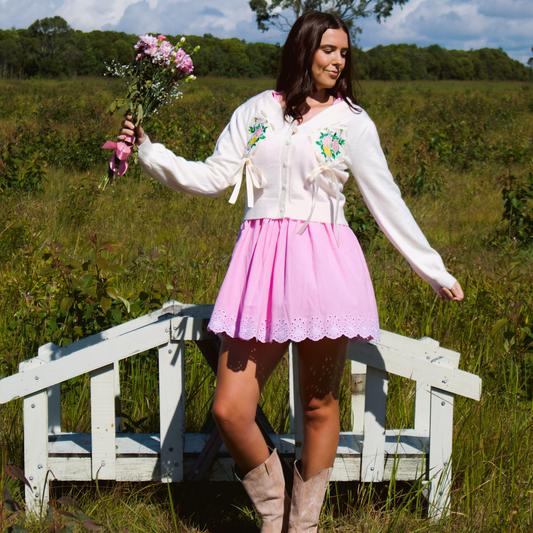 Model wearing a soft white-cream cardigan featuring delicate floral embroidery and bow details, adding a cozy and feminine touch to the look.