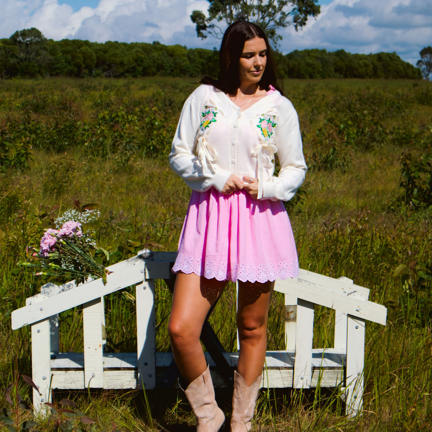 Model wearing a soft white-cream cardigan featuring delicate floral embroidery and bow details, adding a cozy and feminine touch to the look