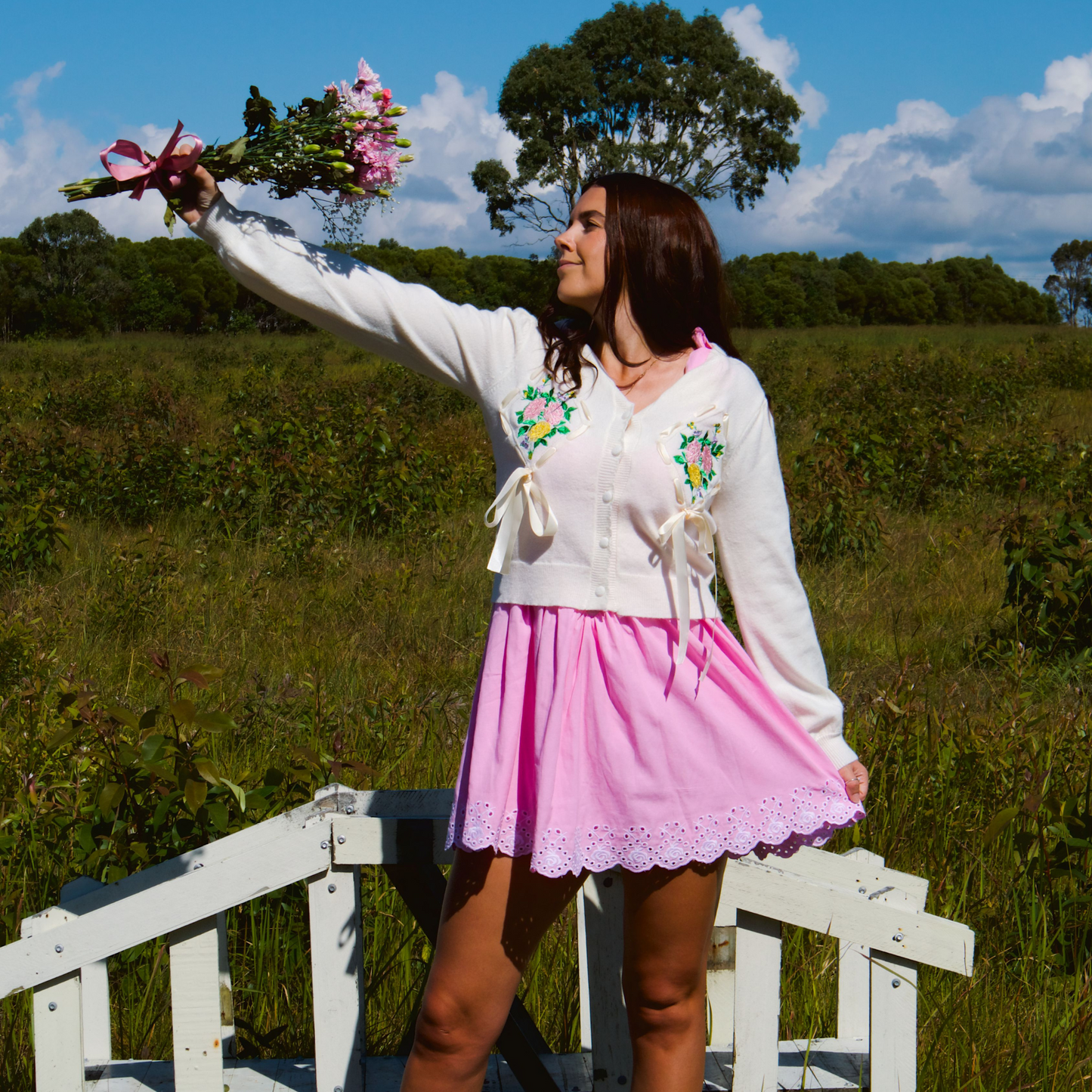 Model wearing a soft white-cream cardigan featuring delicate floral embroidery and bow details, adding a cozy and feminine touch to the look