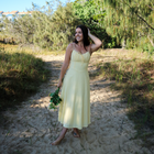 Woman in a light yellow dress standing on a sandy path with greenery around