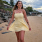 Woman in a yellow dress standing on a beach with a cloudy sky.