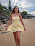 Woman in a yellow dress standing on a beach with a cloudy sky.