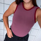 Woman wearing a maroon tank top with red trim in a tiled room.