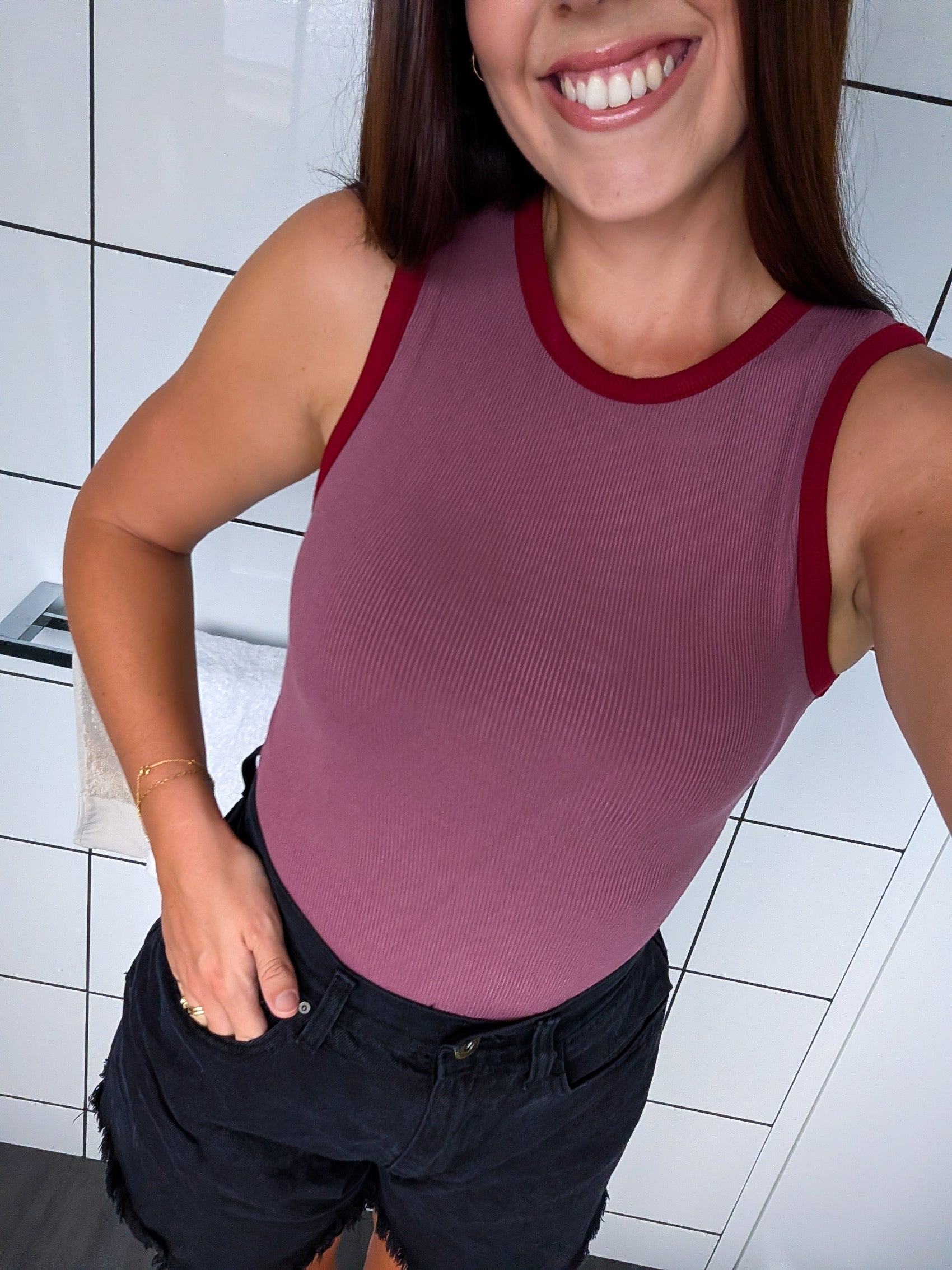 Woman wearing a maroon tank top with red trim in a tiled room.