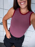 Woman wearing a maroon tank top with red trim in a tiled room.