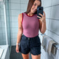 Woman taking a mirror selfie in a bathroom wearing a pink tank top and black shorts.