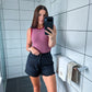 Woman taking a mirror selfie in a bathroom wearing a pink top and black shorts.