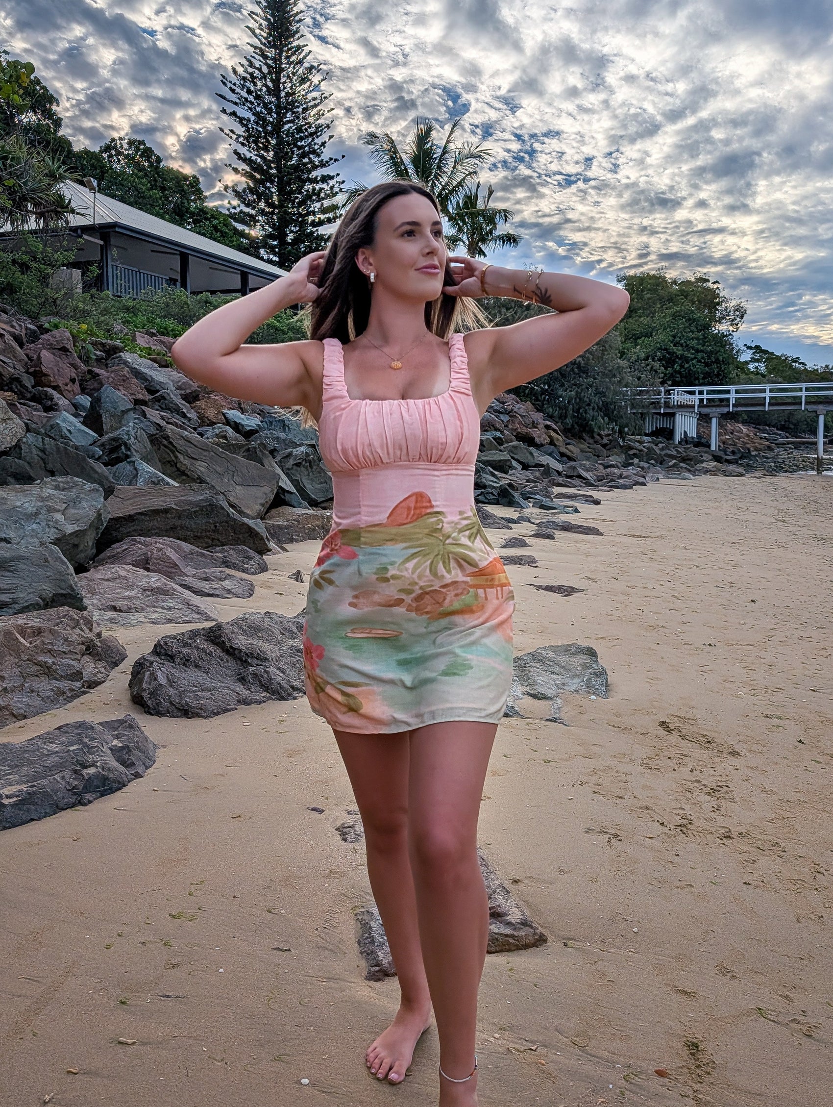 Woman in a colorful dress standing on a beach with rocks and trees in the background