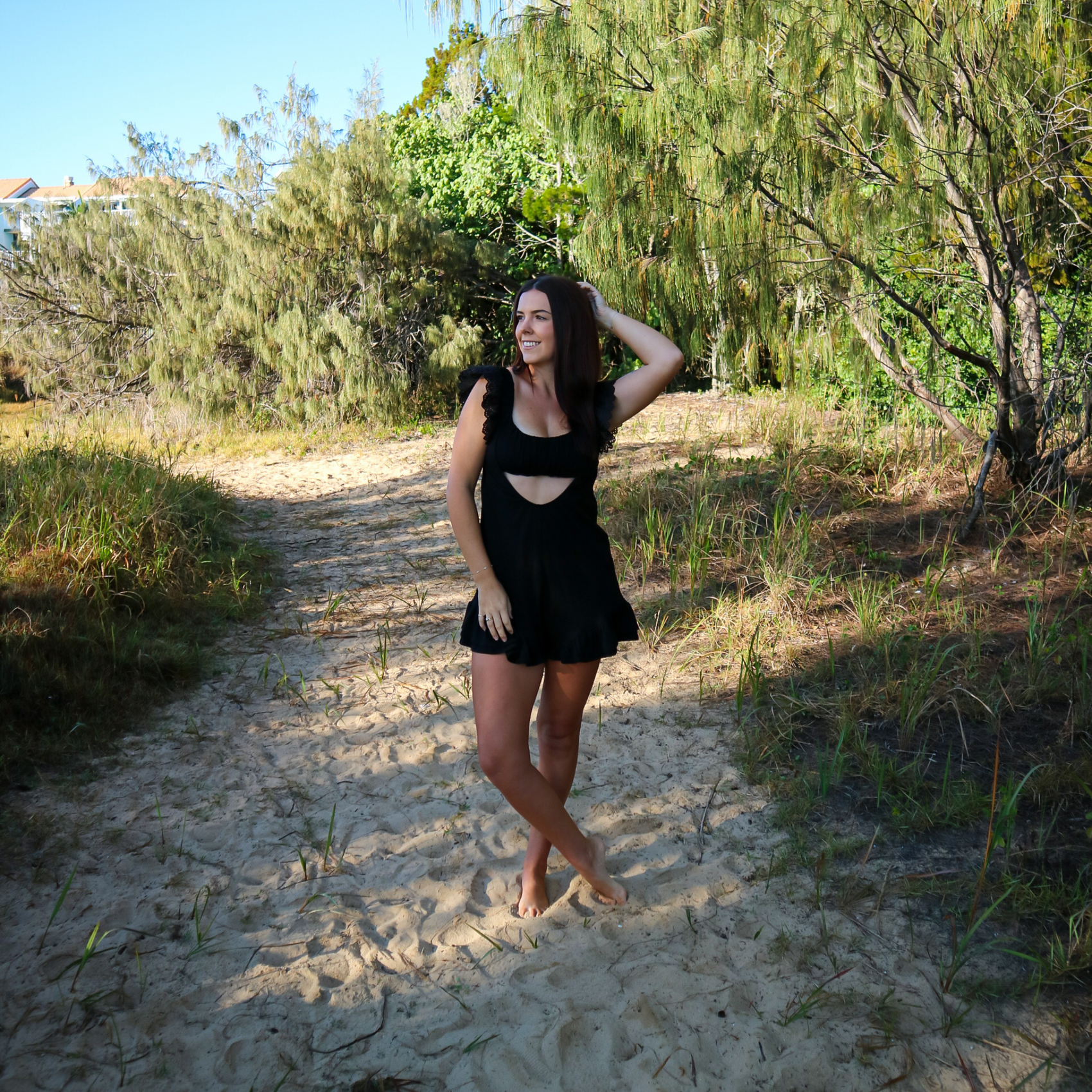 Woman in a black romper standing on a sandy path with trees in the background