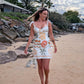 Woman in a floral dress walking on a beach with rocks and trees in the background