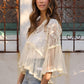 Woman wearing a white lace top and blue jeans standing in front of a decorative metal gate.