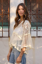 Woman wearing a white lace top and blue jeans standing in front of a decorative metal gate.
