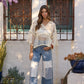 Woman wearing a sheer top and patchwork jeans standing in front of a white wall with decorative metalwork.
