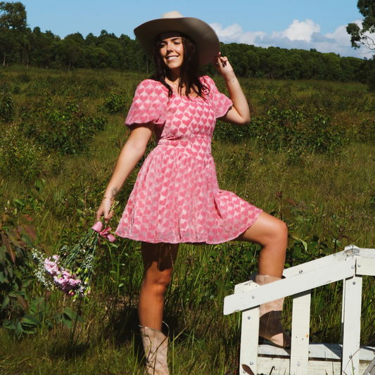 Model wearing a stunning pink dress adorned with heart patterns, featuring puff sleeves and a flattering, romantic silhouette.