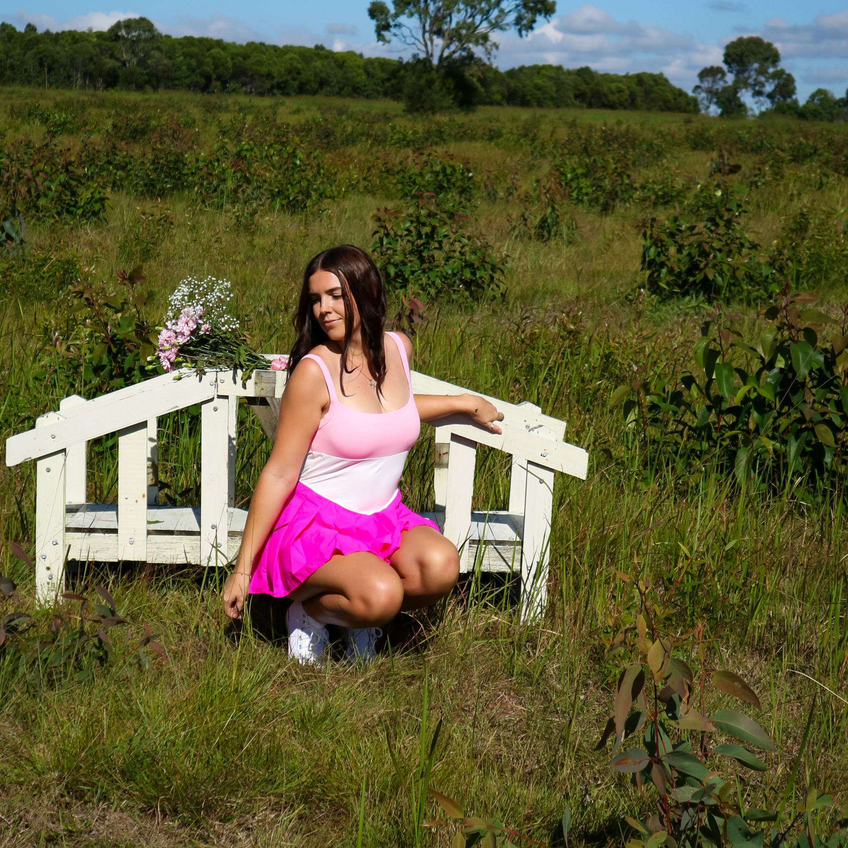 Woman in a pink sports dress sitting on a white bench in a grassy field.