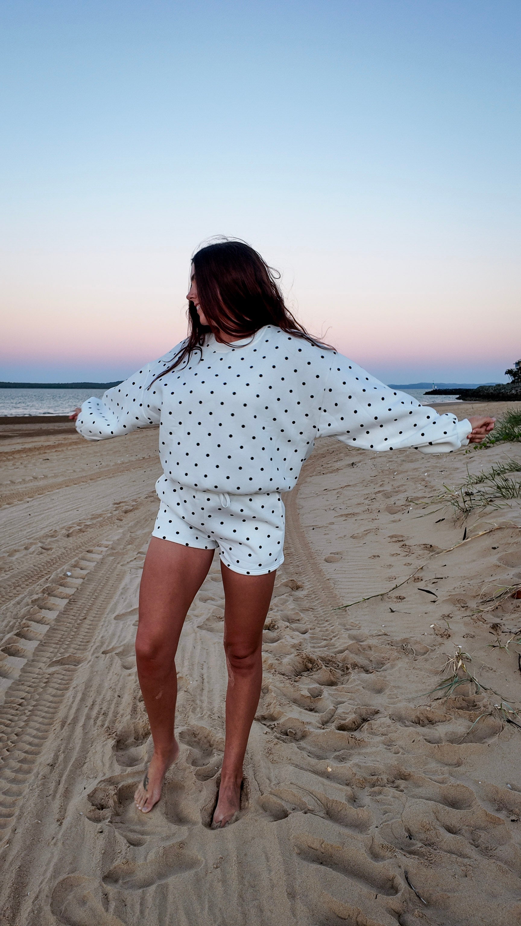 Woman in a polka dot outfit standing on a beach at sunset
