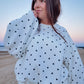 Woman wearing a white polka dot outfit standing on a beach at sunset.