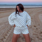 Woman in a polka dot outfit standing on a beach at sunset.