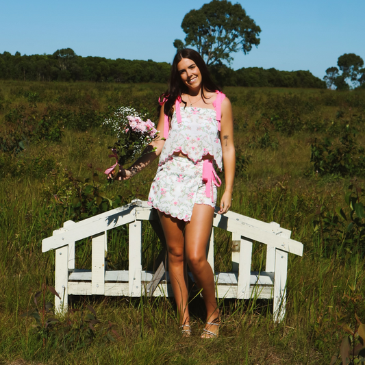 Model wearing a two-piece set featuring a singlet with adjustable straps and matching shorts, designed with a white floral print and soft pink accents for a light, feminine look.