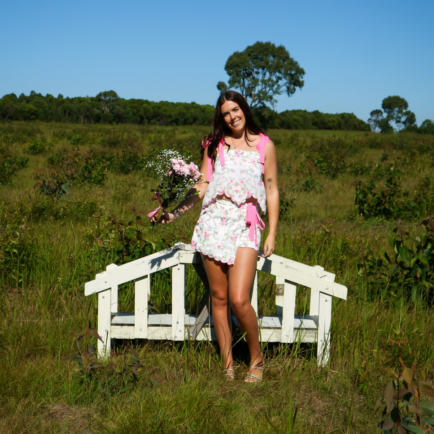 Woman in a floral set standing on a wooden bridge in a grassy field