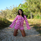 Woman wearing a pink and white chevron patterned dress on a sandy path with greenery in the background