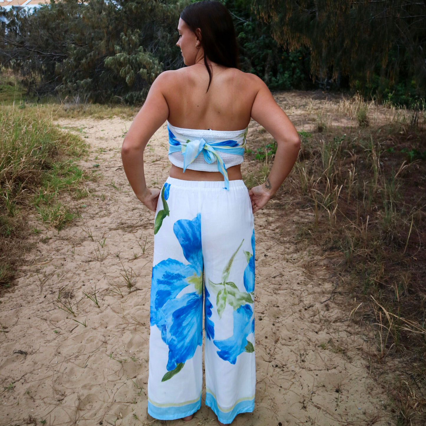Woman wearing a blue floral outfit standing on a sand path with greenery around.
