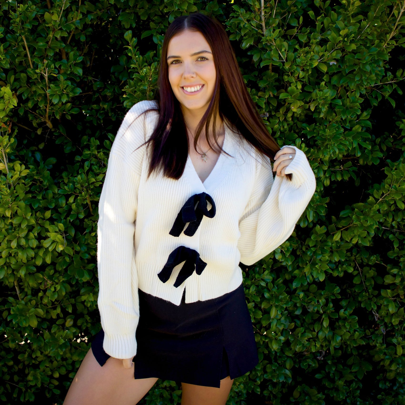 Woman wearing a white sweater with black panther designs against a green bush background