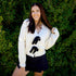 Woman wearing a white sweater with black panther designs against a green bush background