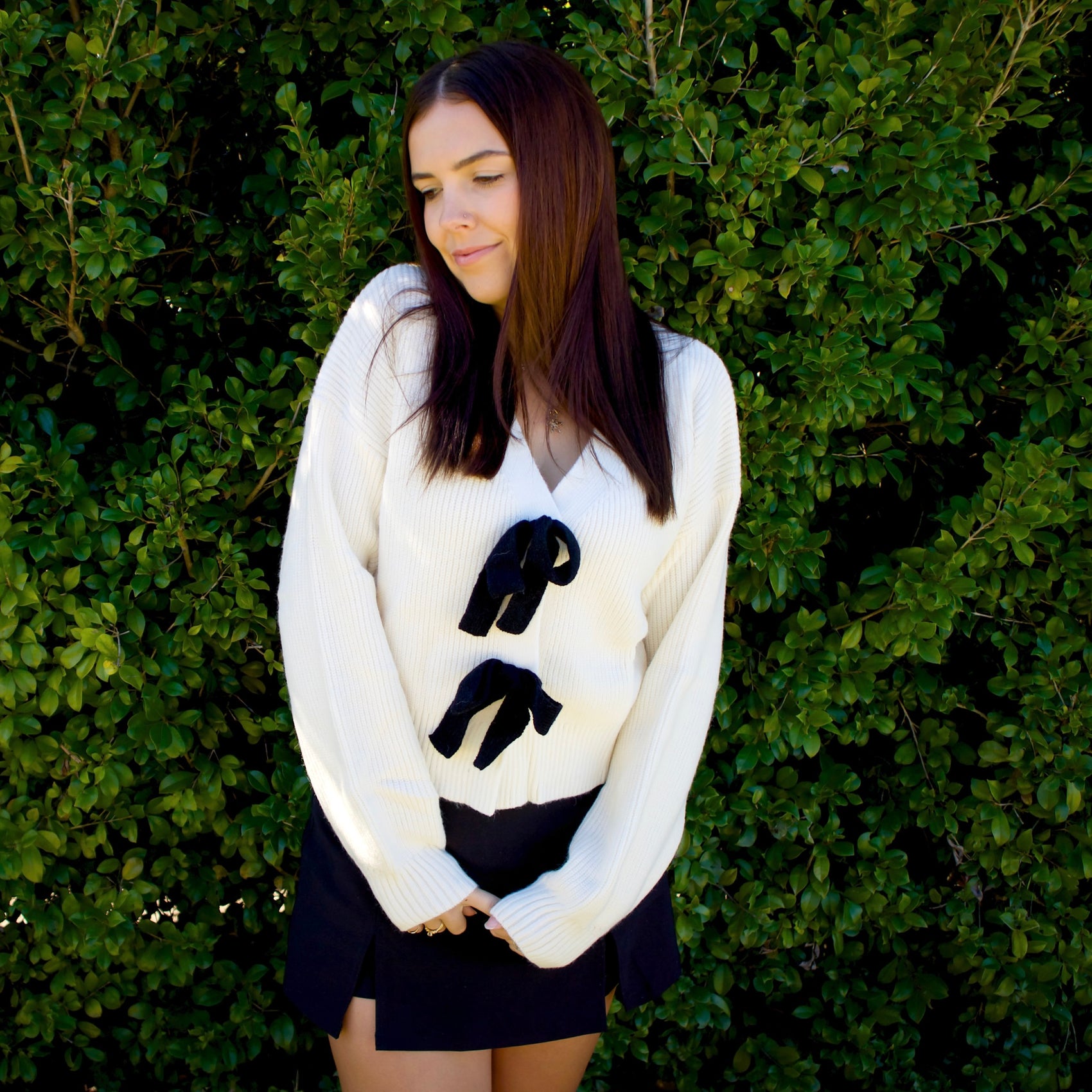 Woman wearing a white cardigan with black bow ties against a green leafy background