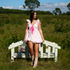 Woman in a pink dress standing next to a white bench in a grassy field