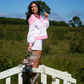 Woman in a pink and white outfit standing on a wooden bridge in a field