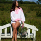 Woman in a white and pink outfit sitting on a wooden bench in a field